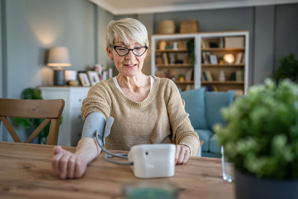 An older woman measuring her blood pressure using an at-home blood pressure machine after experiencing hypertension symptoms.