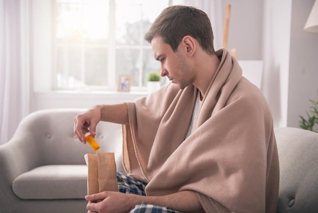 Person checking their delivered prescription while sitting on the couch with a blanket over their shoulders.