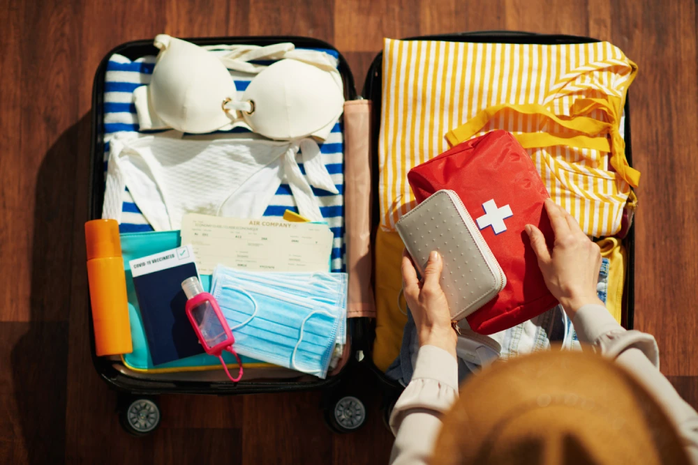a woman packing a travel first aid kit in her luggage