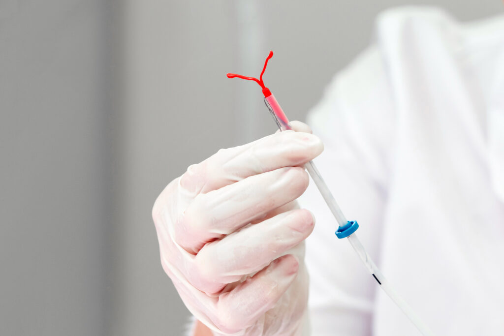 A pharmacist is wearing a glove and holding an IUD device. 
