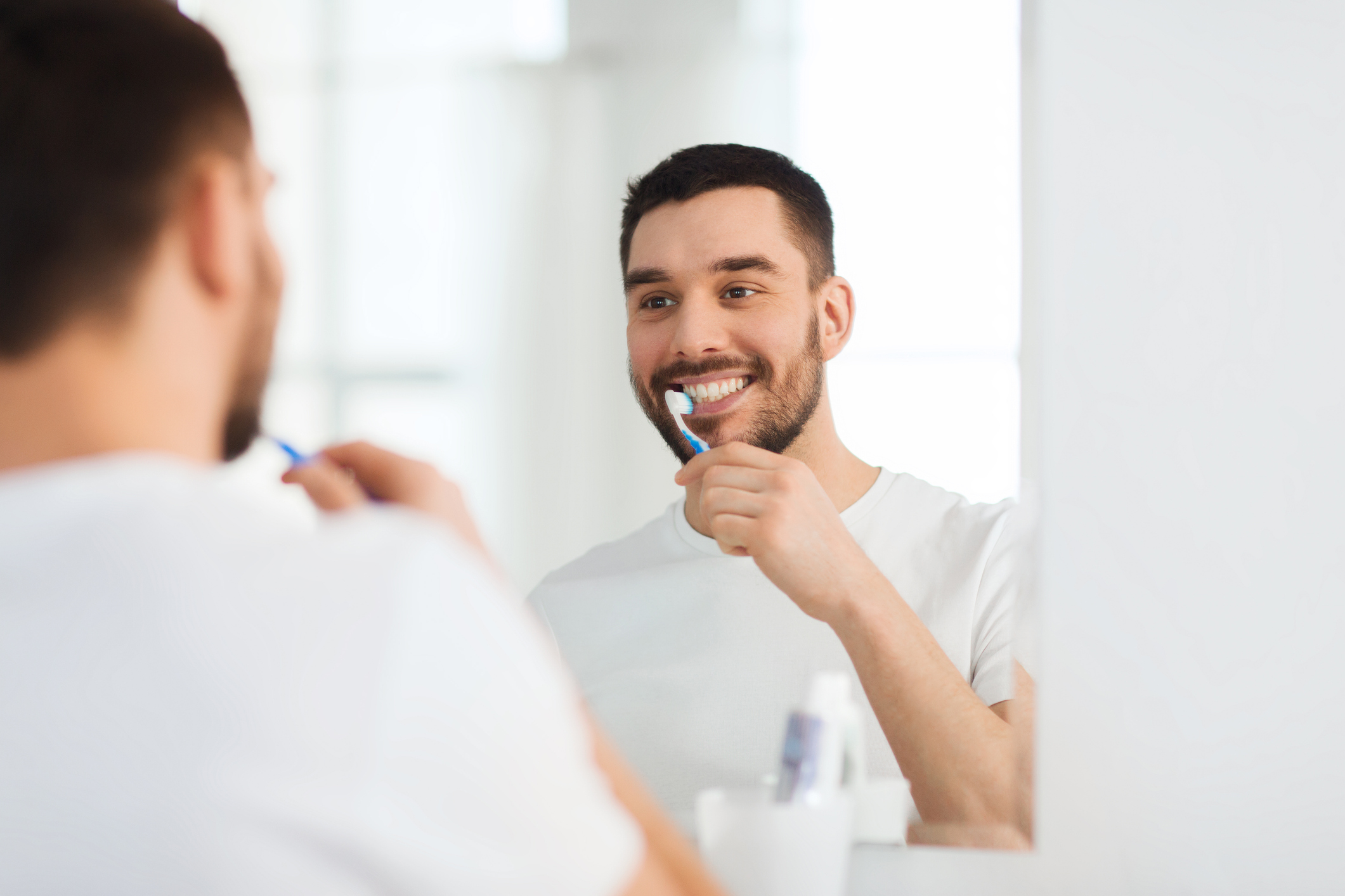 A young man looks in the mirror while brushing his teeth.