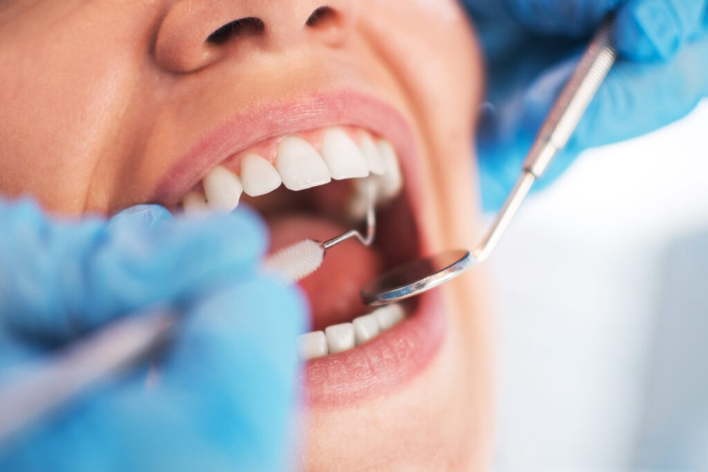 A dentist is examining a woman's teeth with dental instruments. 