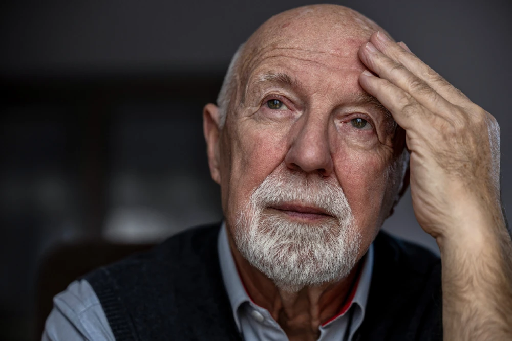 older man with parkinson's disease with his hand on his forehead