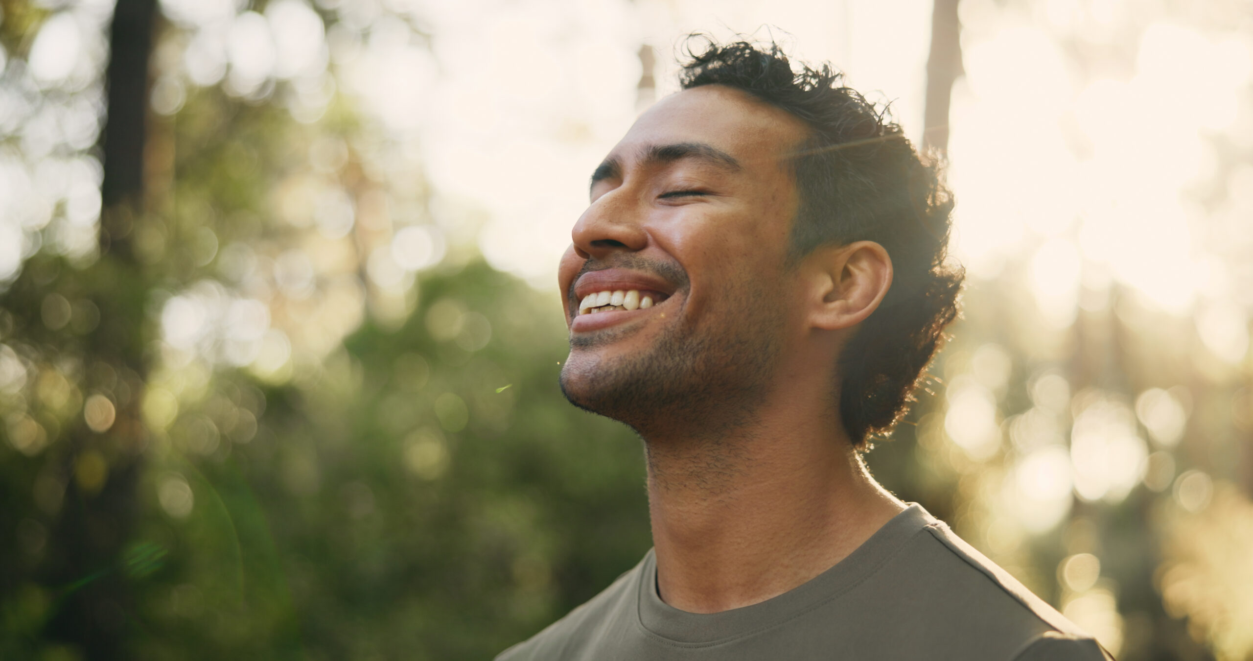 A young man is facing up at the sun with his eyes closed, smiling