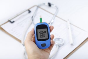 Hand holding a blood glucose meter measuring blood sugar the background is a stethoscope and chart file