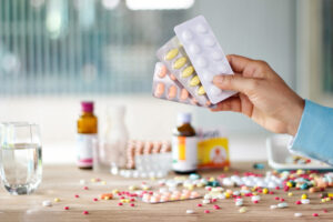 Hand holding medicines pill pack with colorful drugs spread on w