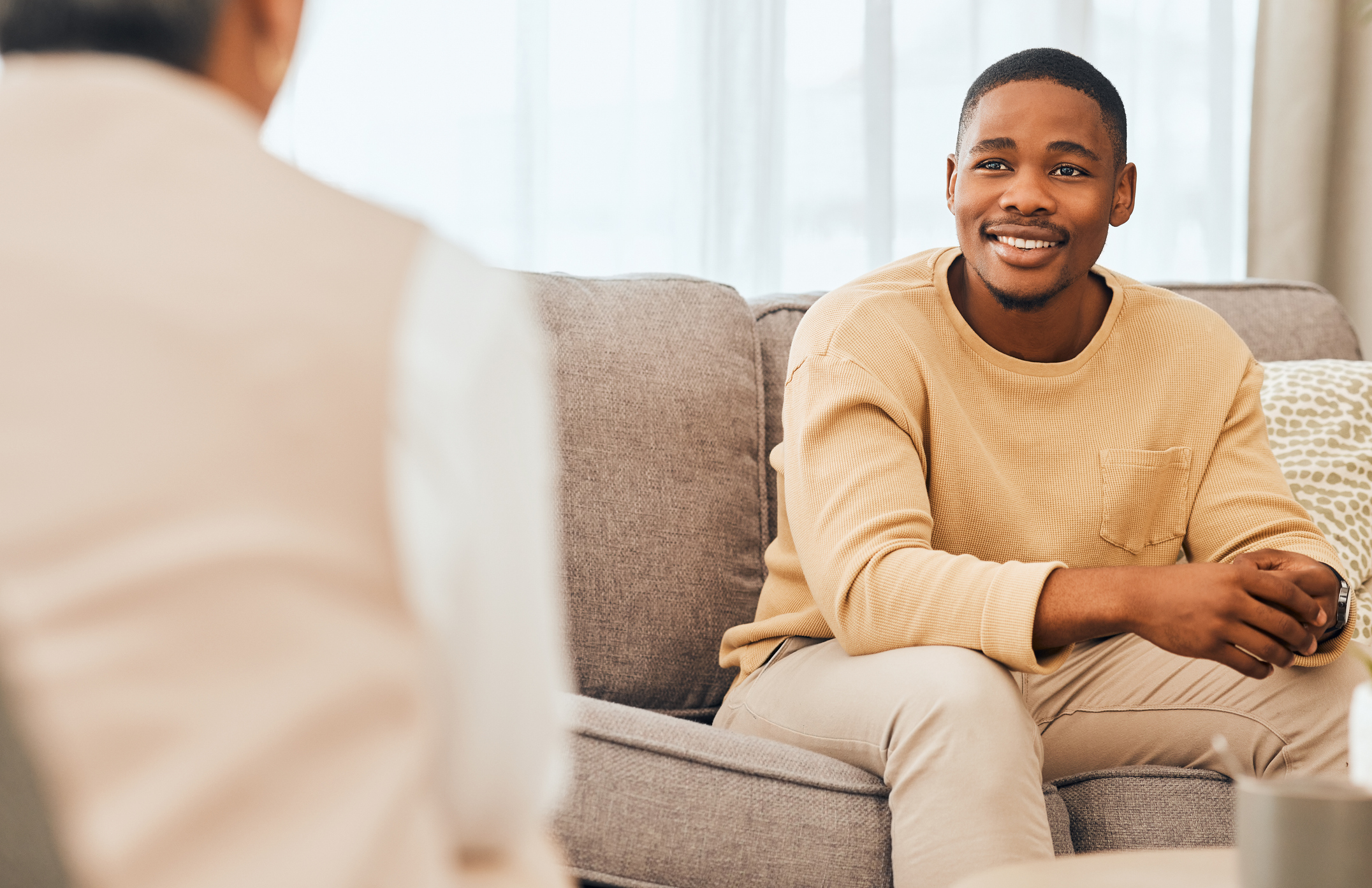 A young smiles as he sits on the couch in a therapist's office.