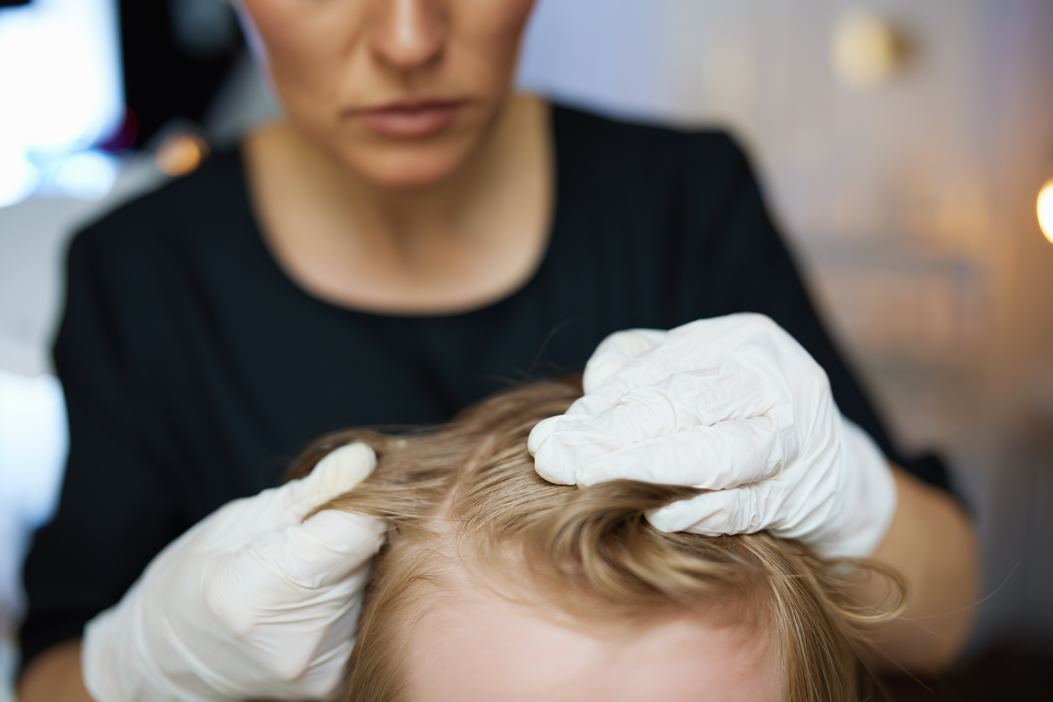 A woman wears gloves as she examines her child's head for lice.