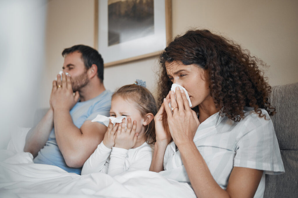 Influenza 101: Prevention, Symptoms, and Treatment Options 1 Une mère, un père et leur enfant, tous atteints de la grippe, sont assis ensemble sur le canapé et se mouchent.