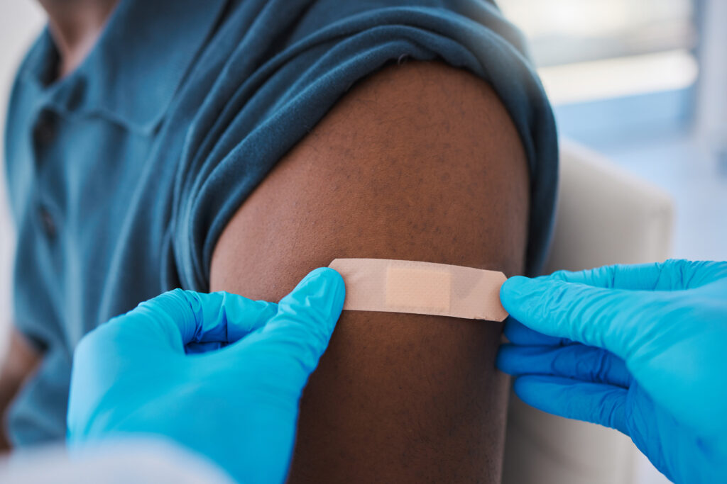 A pharmacist wears gloves while placing a bandage on the vaccination site on a person's arm. 