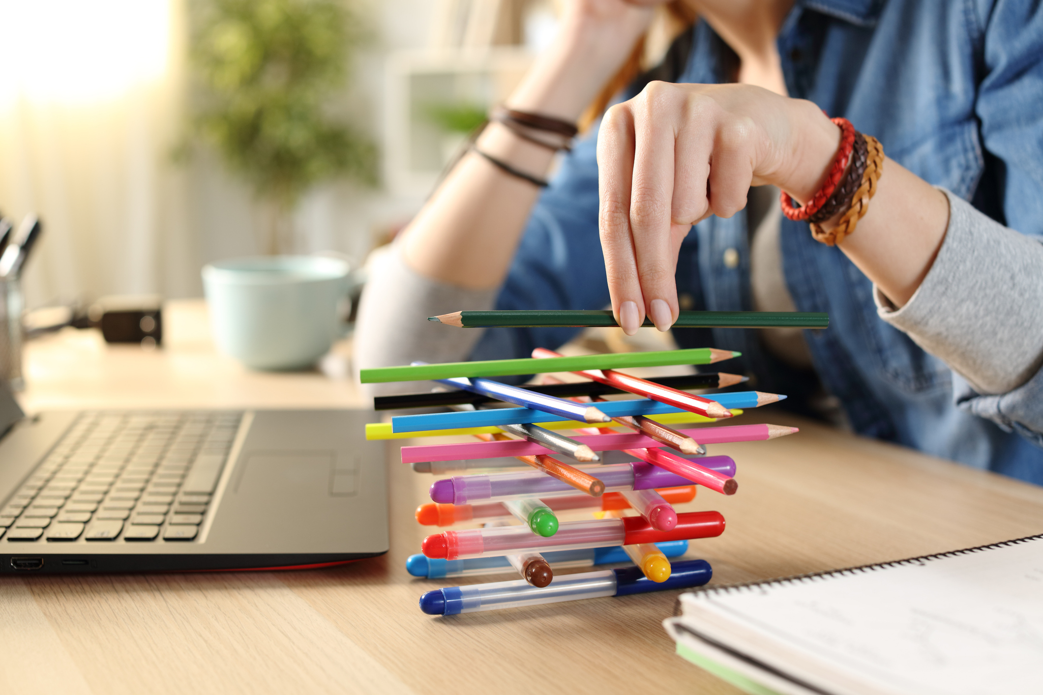 Instead of working on her laptop, a woman is distracted by stacking pens and pencils.